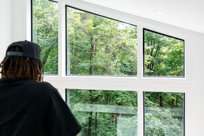 Ein Zimmer mit großen Fenstern und Blick auf ein bewaldetes Gebiet.