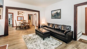 A living room with a leather sofa, a dining table with chairs, and a staircase leading to another room.