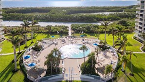 A resort with a central pool, palm trees, and a view of the ocean. - Stylish Front Corner Beachfront Resort | 5⭐️ Local Host | Balcony | Views (Marco Island)