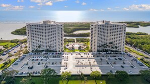 A high-rise hotel with a central courtyard, parking lot, and views of the sea and greenery. - Stylish Front Corner Beachfront Resort | 5⭐️ Local Host | Balcony | Views (Marco Island)