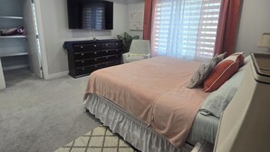 A bedroom with a large bed, a dresser, a TV mounted on the wall, and a ceiling light fixture.