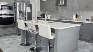 A modern kitchen with stainless steel appliances, a large island with bar stools, and a tiled backsplash.