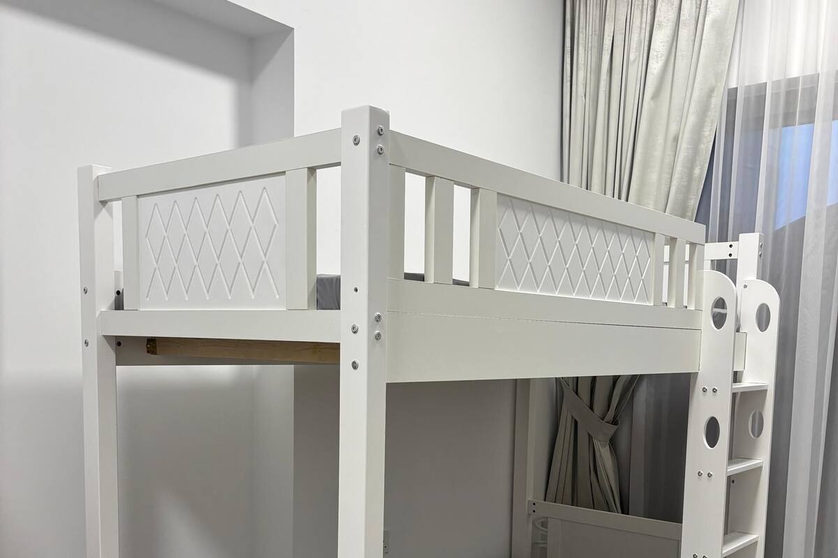 Un lit superposé avec une échelle et une étagère, une table de chevet en bois et une fenêtre avec des rideaux.