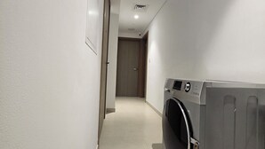 Ein Waschraum mit einer grauen Waschmaschine, einer Tür zu einem anderen Raum und einem gefliesten Boden.