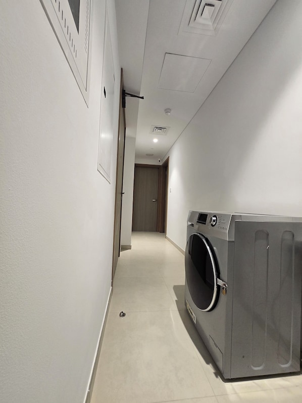 A laundry room with a gray washing machine, a door leading to another room, and a tiled floor.