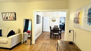 A living room with a sofa, a dining table with chairs, a mirror, and a painting on the wall.