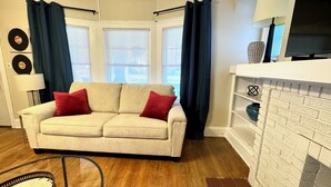 A living room with a beige sofa, red cushions, a glass coffee table, a lamp, and a brick fireplace.