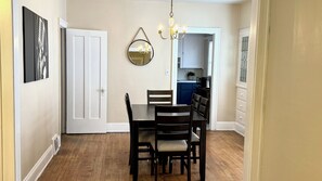Un comedor con una mesa y sillas de madera, una araña, un espejo y una cocina visible a través de una puerta abierta.