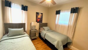Un dormitorio con dos camas, una mesita de noche con lámpara y un ventilador de techo.