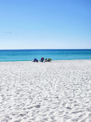 Une plage de sable avec trois chaises de plage et un parasol bleu.