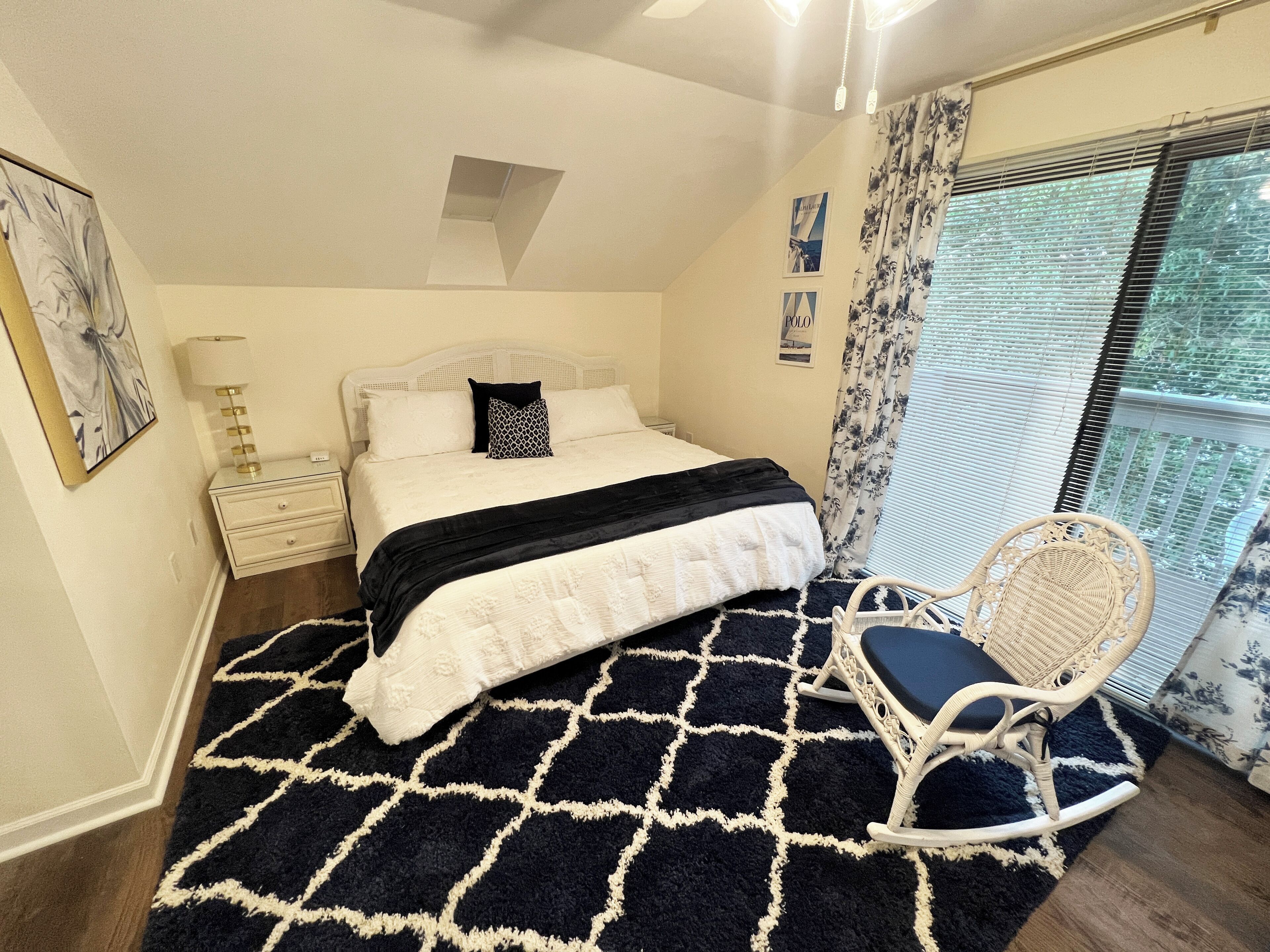 Een slaapkamer met een bed, een stoel, een nachtkastje, een lamp en een raam met gordijnen.
