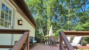 A wooden deck with outdoor seating and a view of trees. - Cozy Modern Cabin in the Woods (Hawley)