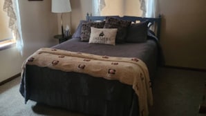 A bedroom with a bed, a nightstand, a lamp, and two windows with curtains.
