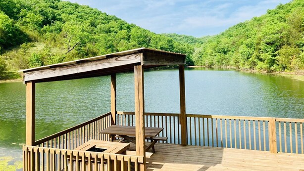 A wooden deck with a gazebo and picnic table overlooking a calm lake, surrounded by lush green hills. - 4BR Connected Condo Near Silver Dollar City | Great for Groups | NCH 7 7-8 (Reeds Spring)