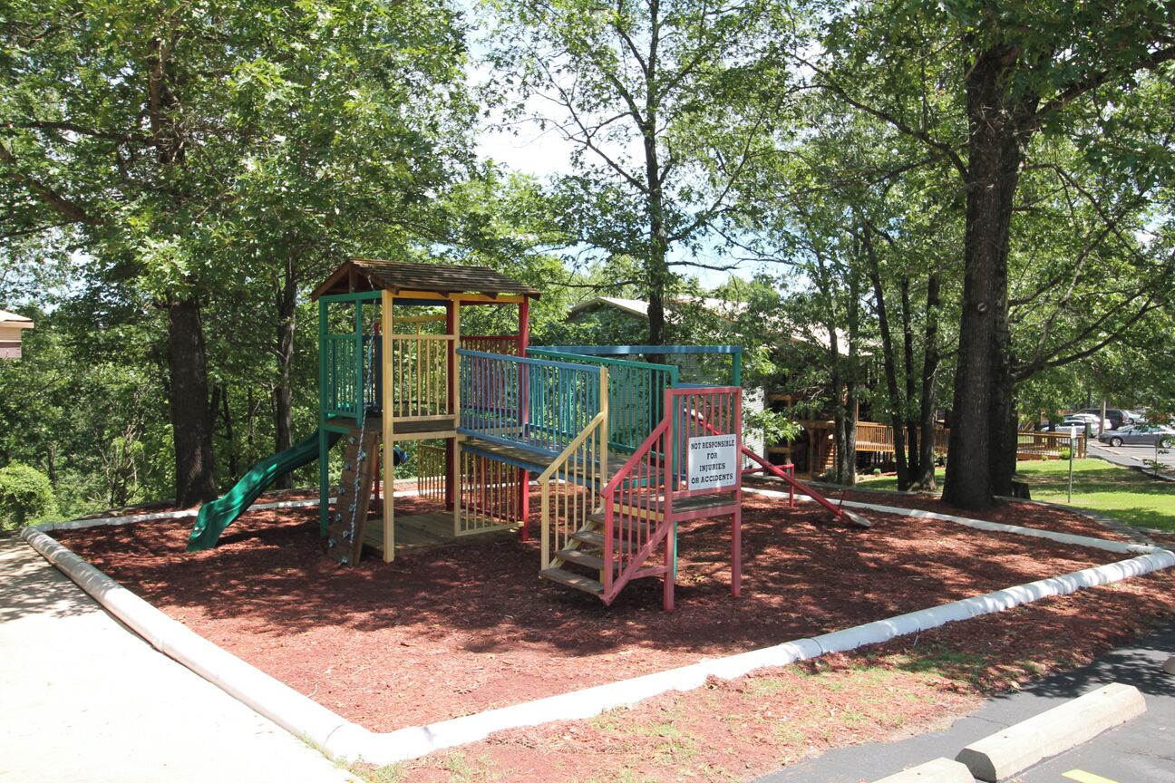 Ein Spielplatz mit Rutsche und Klettergerüsten, umgeben von Bäumen.