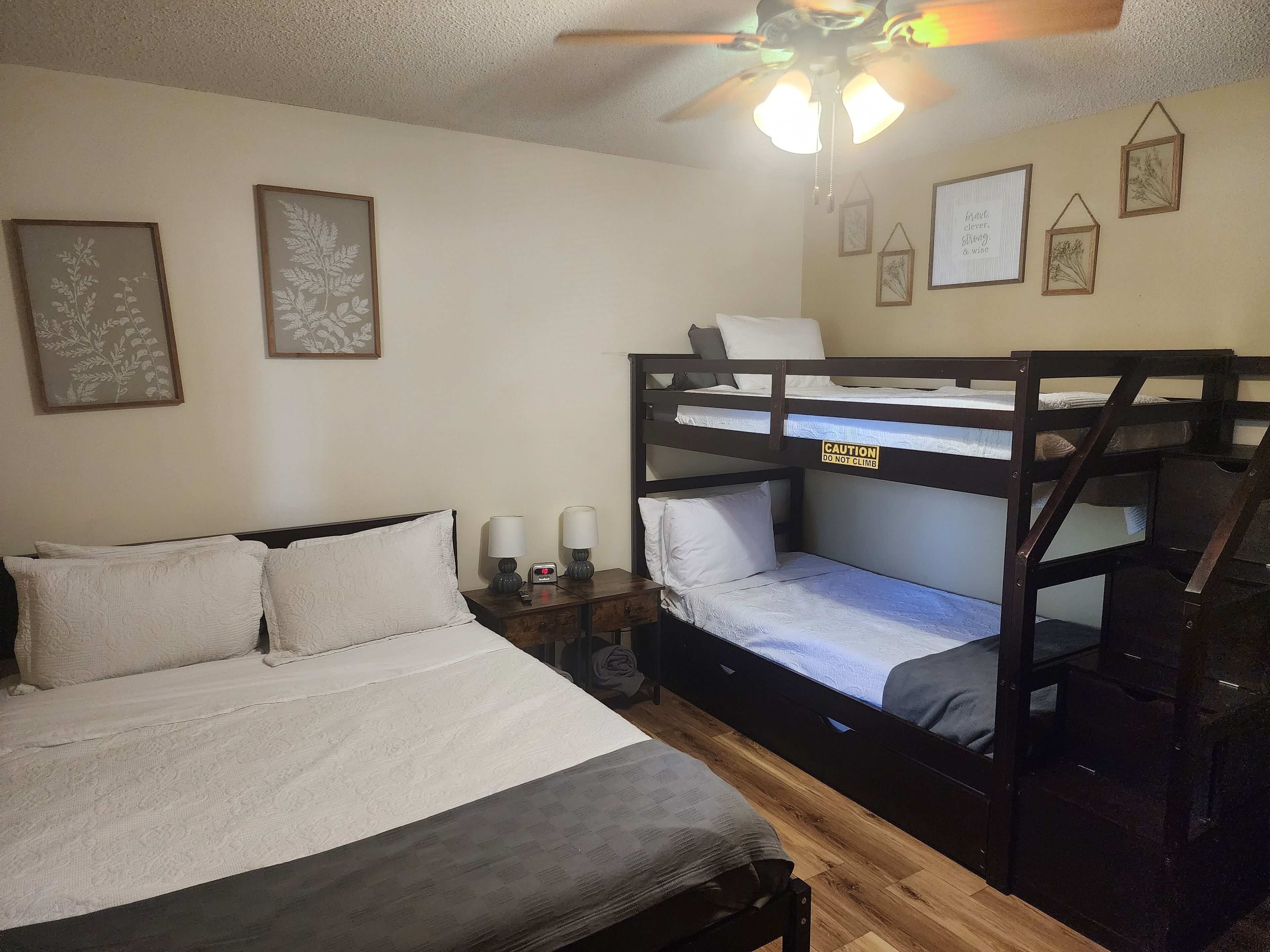 Habitación con literas, ventilador de techo, mesitas de noche con lámparas e impresiones botánicas enmarcadas en las paredes.