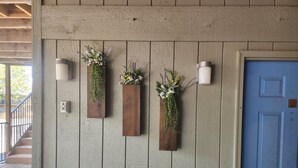 A wooden wall with three vertical planters containing flowers and greenery, a white electrical box, and a blue door with a welcome sign. - 4BR Connected Condo Near Silver Dollar City | Great for Groups | NCH 7 7-8 (Reeds Spring)