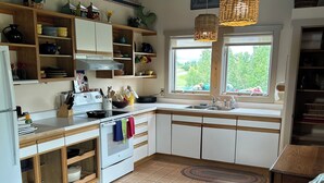 A kitchen with wooden cabinets, a stove, a sink, and a window with a view of greenery.