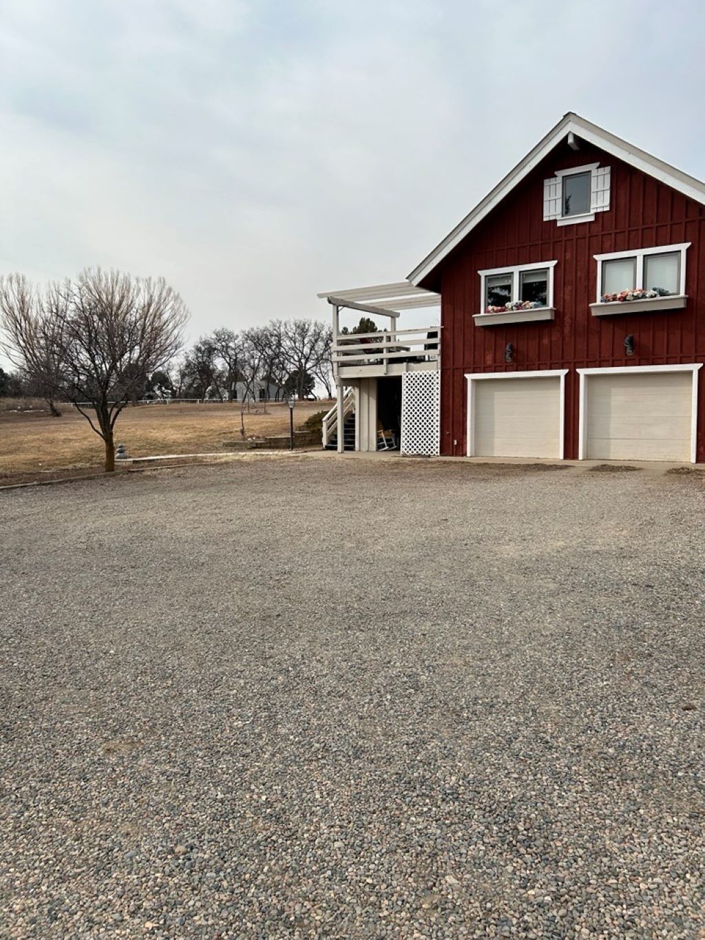 A red barn with two garage doors, a covered porch, and a gravel driveway.
