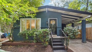 A house with a covered porch, a front door, and a small garden area with plants and a wooden planter.