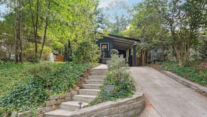 A stone staircase leading to a dark-colored house with a covered porch, surrounded by lush greenery.