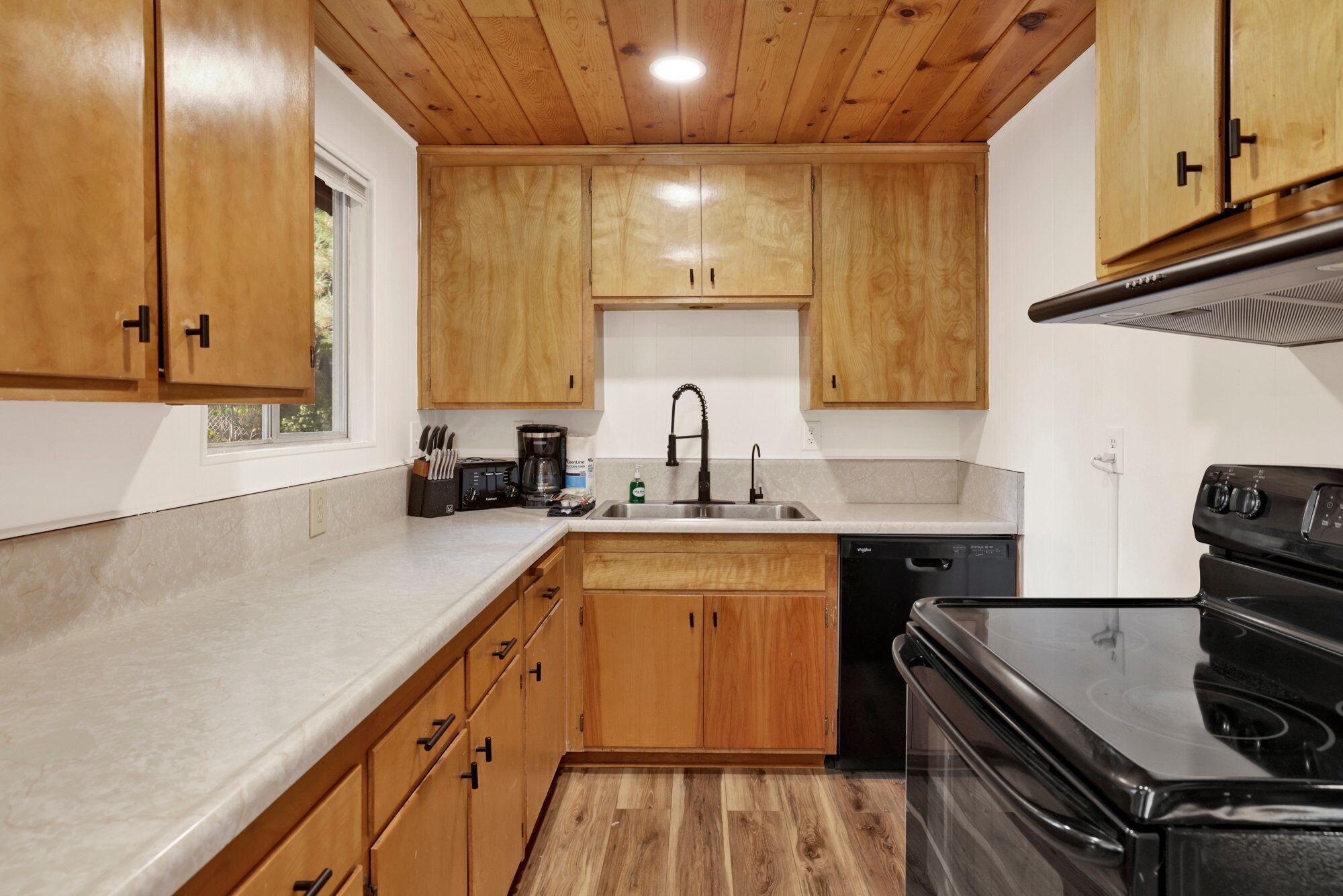 Una cocina con armarios de madera, un lavamanos de acero inoxidable, una cafetera y un lavavajillas.