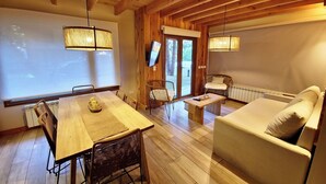 Una habitación acogedora con una mesa de madera, sillas, un sofá y un televisor en la pared.