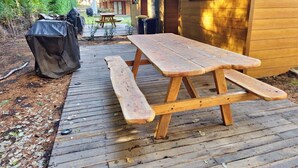 Una terraza de madera con una mesa de picnic, rodeada de cabañas de madera.