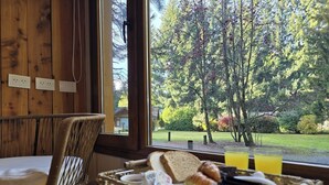 Bandeja de desayuno con pan, mantequilla, mermelada y una bebida, sobre una mesa con vista a un área boscosa.