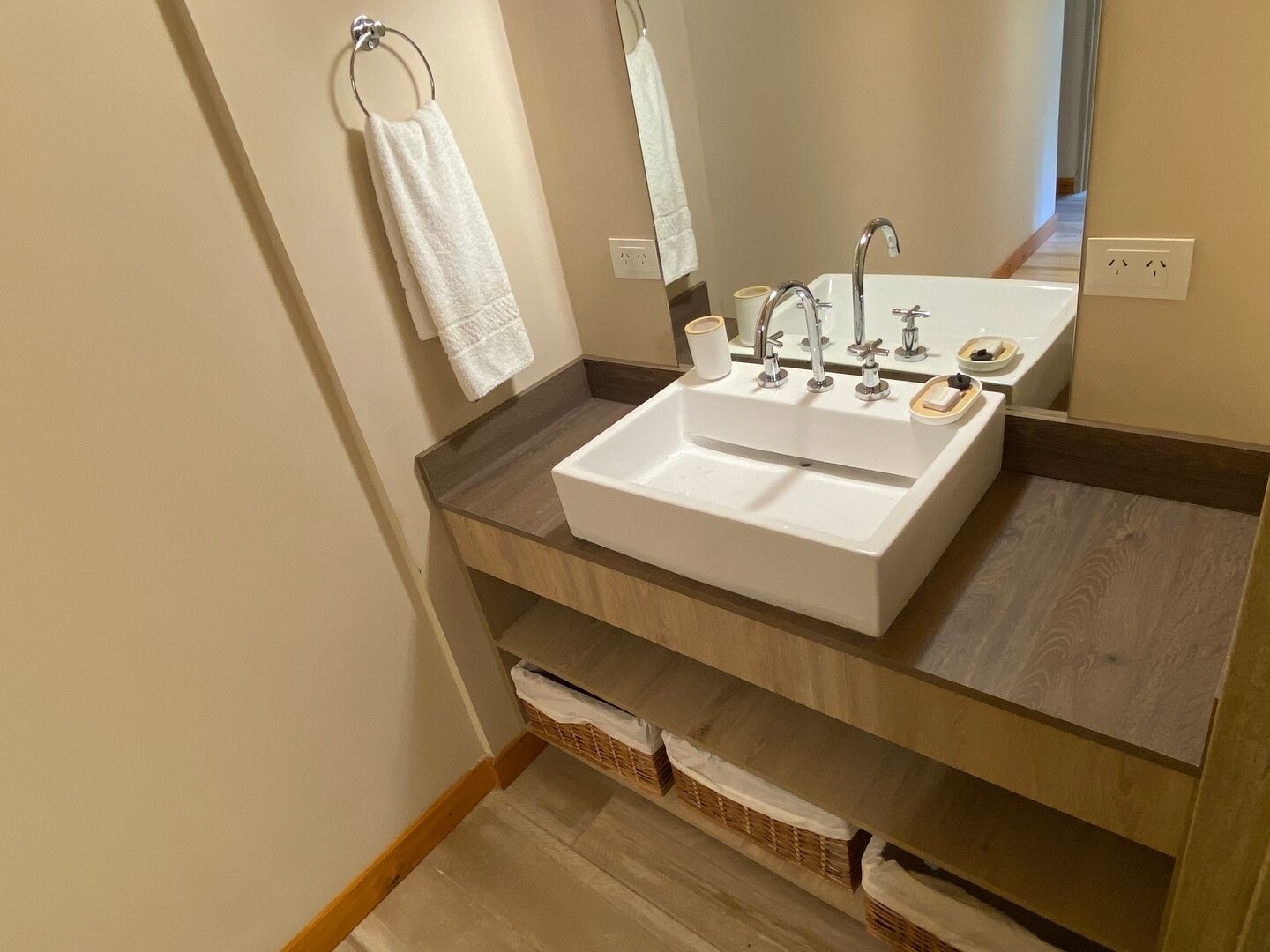 A bathroom with a white sink, two faucets, a mirror, and a towel rack.