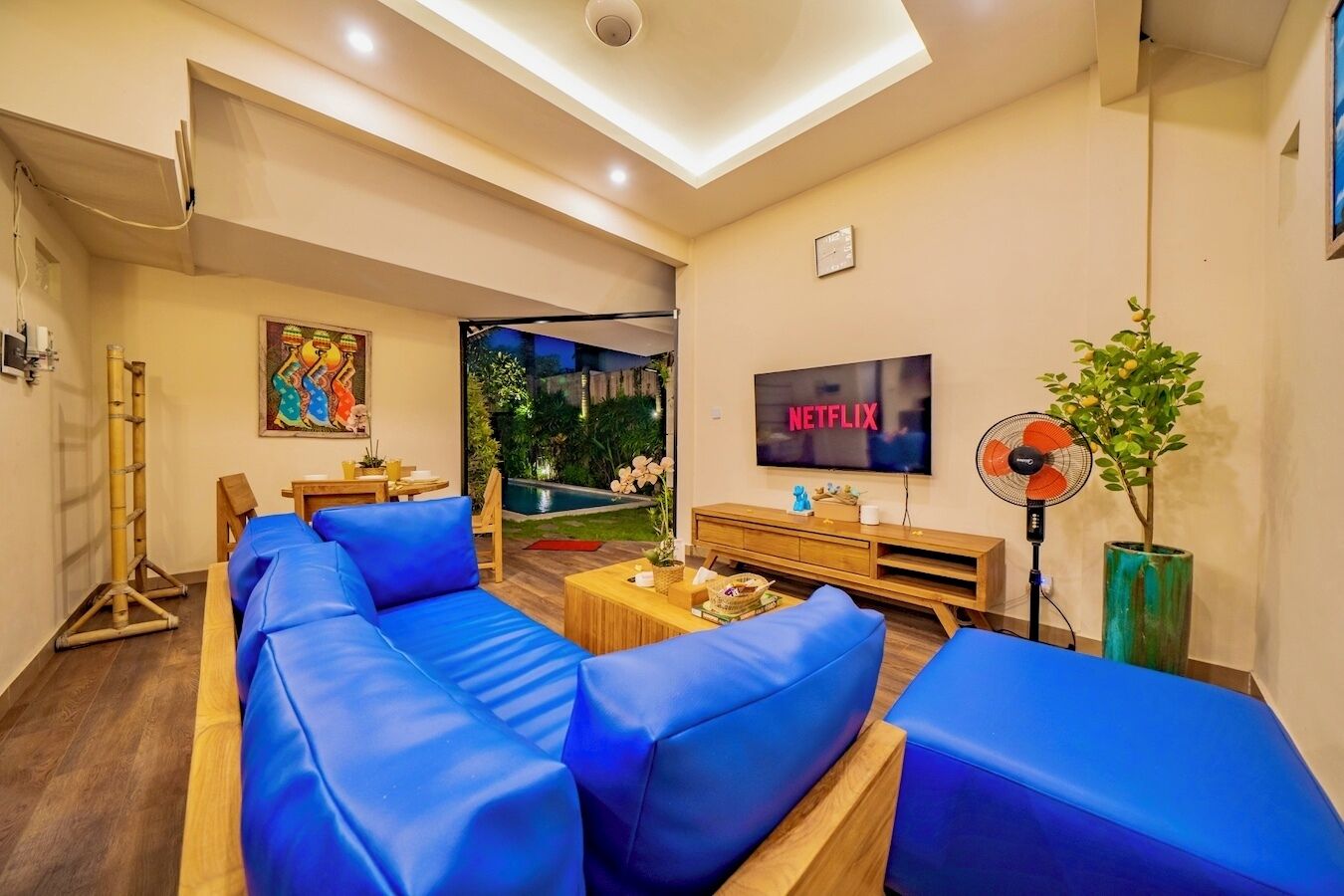 A modern living room with a large sofa set, a flat-screen TV, a fan, and a small table with decorative items.