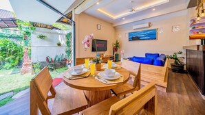 Un salon moderne avec une table à manger en bois, préparée pour quatre personnes, un canapé bleu et un téléviseur fixé au mur.