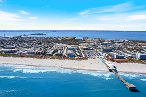 Vista aérea de un pueblo costero con playa, muelle y diversos edificios, incluyendo hoteles y zonas residenciales.
