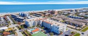Vue aérienne d’un hôtel situé sur la côte, composé de plusieurs bâtiments, avec un parking et une plage en arrière-plan.
