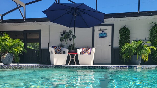 A clear swimming pool with a tiled edge, a white door, and a blue umbrella. - Cozy 2-beds Family Friendly Apt w/ Pool, Full Kitchen in Downtown Kissimmee (Kissimmee)