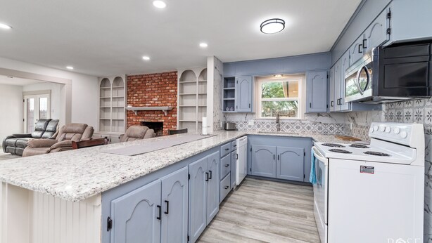 A modern kitchen with blue cabinets, a white stove, and a built-in brick fireplace.