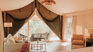A spacious bedroom with a large bed, a seating area with a round table, and a view through a window. - Lantana - Luxury Glamping Tent (Blanco County)