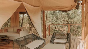 A cozy tented accommodation with a wooden deck, wicker furniture, and a sofa. - Lantana - Luxury Glamping Tent (Blanco County)