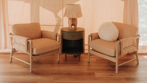 A room with a wooden floor, two beige armchairs, a small round table with a lamp, and a large window with sheer curtains. - Lantana - Luxury Glamping Tent (Blanco County)