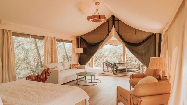 A spacious bedroom with a large bed, a sofa, a chair, and a small table. There is a balcony with a table and chairs. - Lantana - Luxury Glamping Tent (Blanco County)