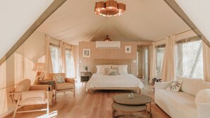 A tent-style room with a bed, two sofas, a round table, and a lamp.
