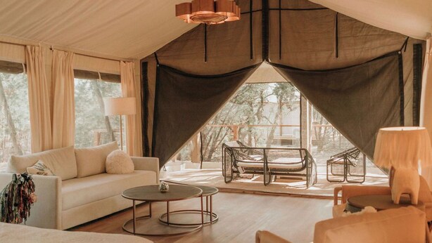 A spacious tented accommodation with a large bed, a sofa, a chair, and a dining area.
