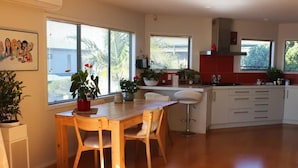 A modern kitchen with wooden cabinets, a dining area with a wooden table and chairs, and large windows with blinds.