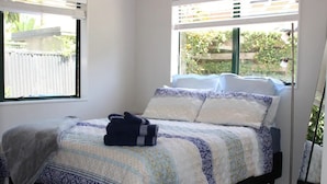 A neatly made bed with a patterned bedspread and pillows, a bedside lamp, and a window with a view of greenery outside.
