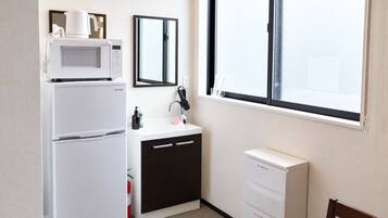 A compact hotel room with a kitchenette, a sink, a mirror, a window, and a chair.