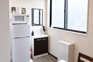 Habitación de hotel compacta con kitchenette, lavamanos, espejo, ventana y una silla.