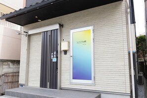 A building with a closed shutter door, a sign reading "SLEEPLAB THE STAY", and a small air conditioning unit mounted on the wall. - SLEEPLAB Asakusa (Sumida-ku)