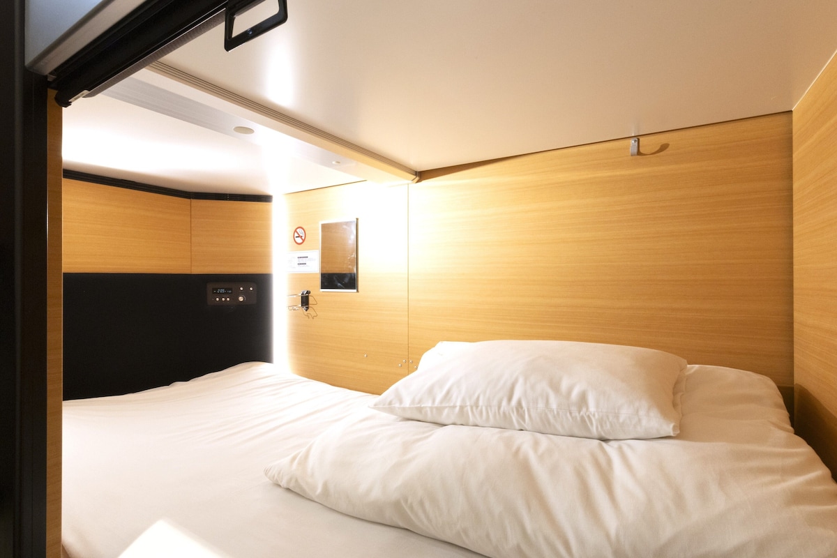 Une chambre d’hôtel avec un lit, une tête de lit en bois, un panneau de commande et un panneau indiquant qu’il est interdit de fumer.