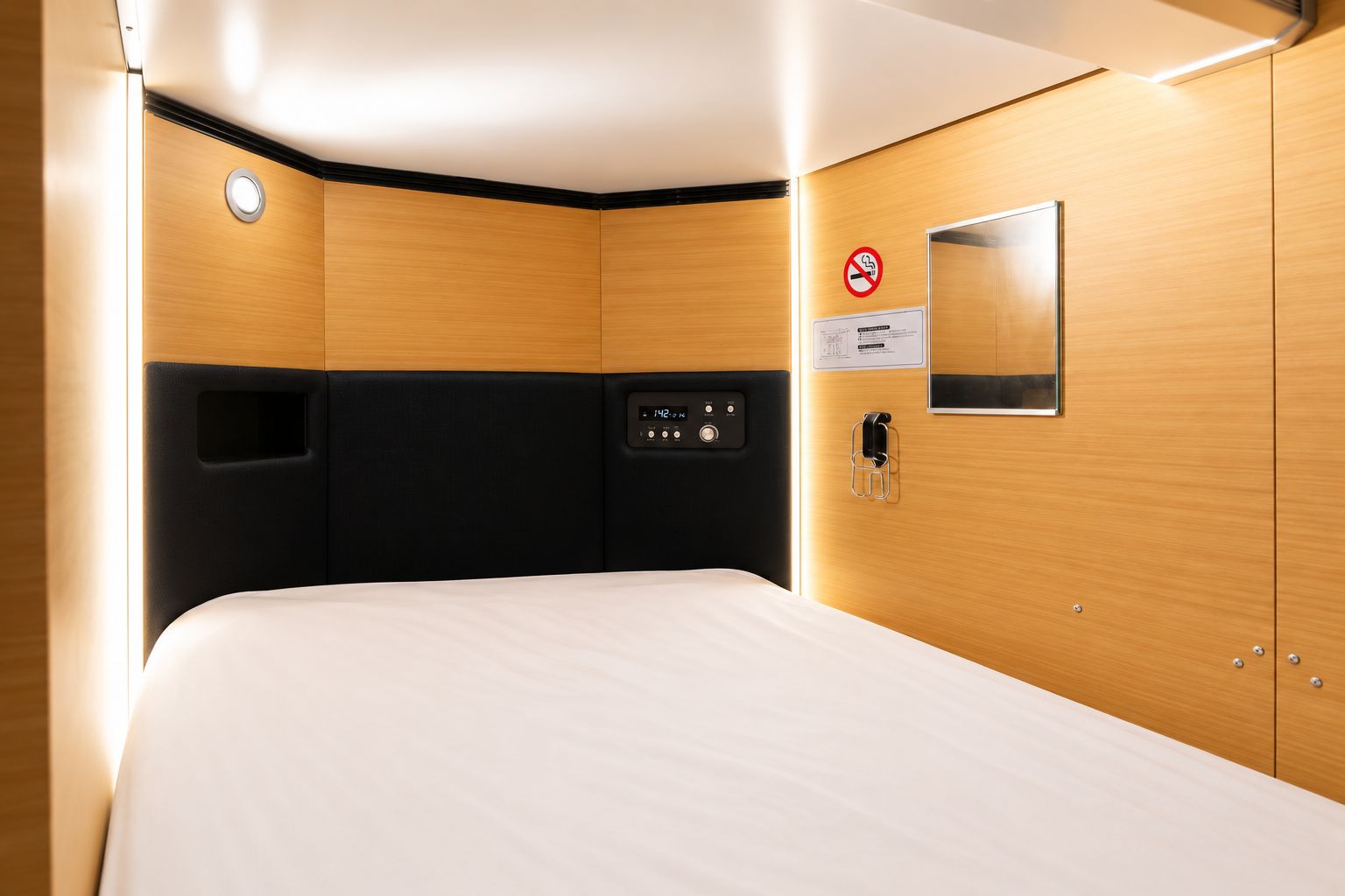 A hotel room with a bed, a control panel, a mirror, and a no-smoking sign.
