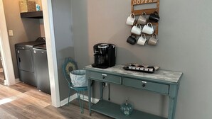 A compact kitchen with a coffee station, a sink, and a teal chair. - corporate comfort suits  (Pocahontas)
